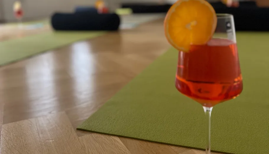 Orange cocktail on yoga mat, wooden floor.