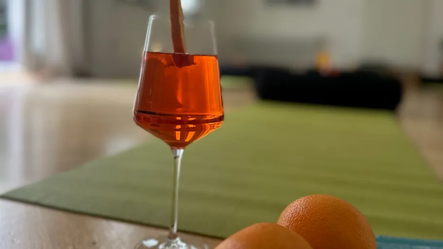Orange drink in glass, oranges nearby, indoor setting.
