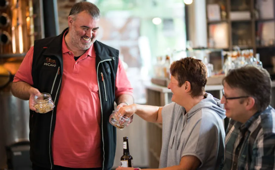 Mann teilt Gläser mit sitzenden Menschen drinnen.