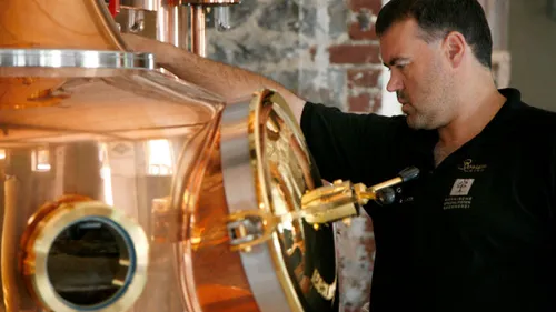 Man examining copper brewing equipment indoors.