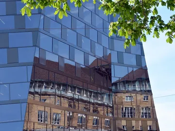 A reflecting building reflects historic architecture under a blue sky.
