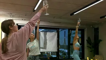 Three women lifting glasses during yoga class.