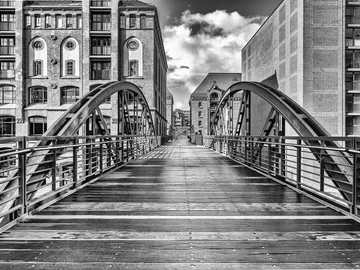 Brücke verbindet historische Gebäude unter wolkigem Himmel.