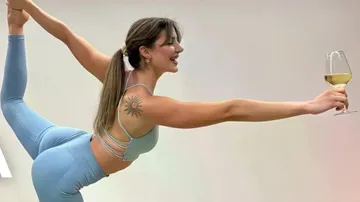 Woman balances holding wine, wearing athletic wear.