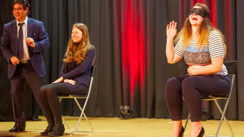 Two blindfolded women on stage with entertainer.