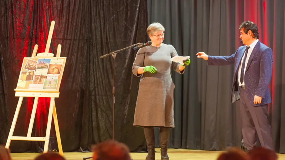 Two people on stage with easel, exchanging an object.