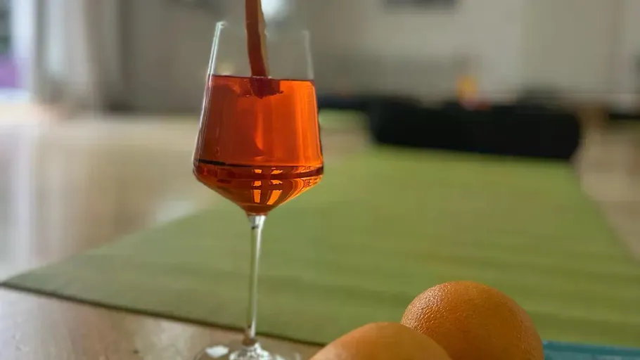 Orange drink in glass, oranges nearby, indoor setting.
