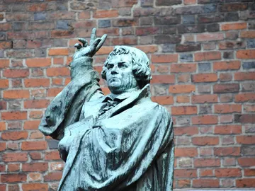 Bronze statue depicts man with raised hand in front of a brick wall.