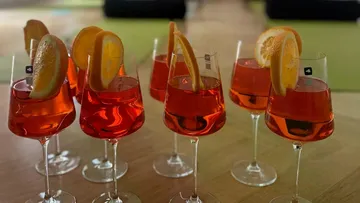 Gläser mit orangenen Getränken und Garnitur auf Tisch.