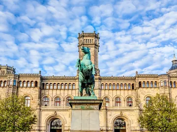 Pferdestatue steht vor einem historischen Gebäude unter Wolken.