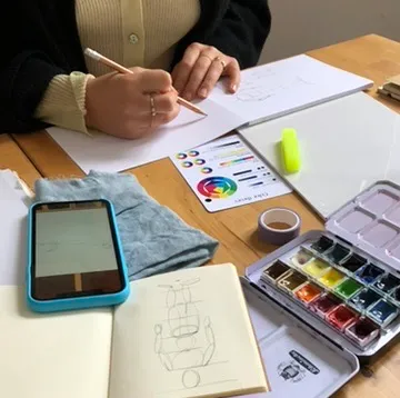 Person zeichnet auf Papier am Tisch.