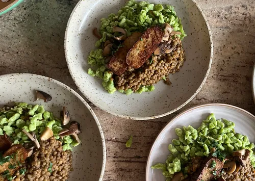 Plates with pasta, lentils, mushrooms, tofu on table.