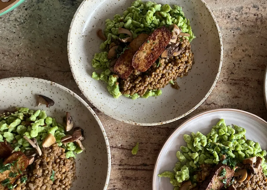Plates with pasta, lentils, mushrooms, tofu on table.