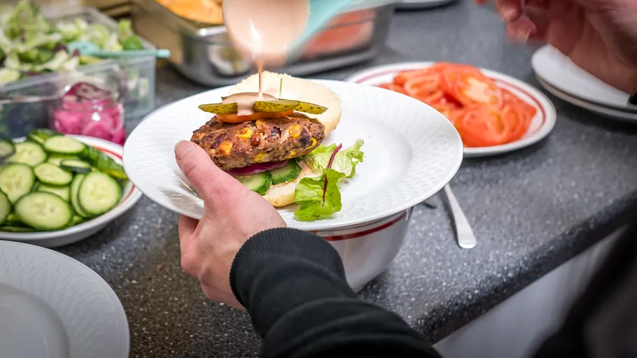 Hands preparing burger with pickles, greens, indoors.
