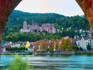 Burg auf Hügel, reflektiert im Fluss, umgeben von Häusern.