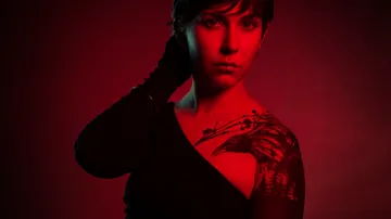 Person in black with raven tattoo, red lighting.