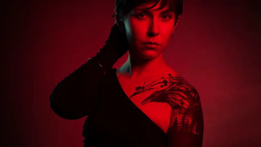 Person in black with raven tattoo, red lighting.