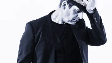 Man adjusting hat, wearing a suit, against white background.
