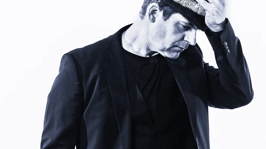 Man adjusting hat, wearing a suit, against white background.