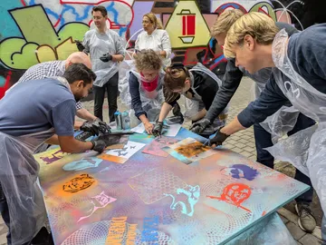 Menschen gestalten Graffiti-Kunst auf großer Leinwand im Freien.