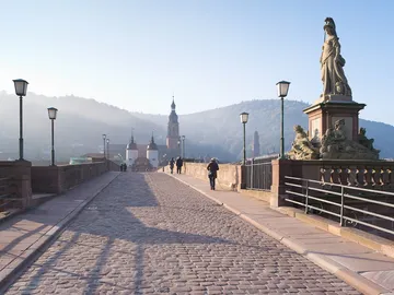 Steinbrücke mit Fußgängern, umgeben von Bergen und Statuen.