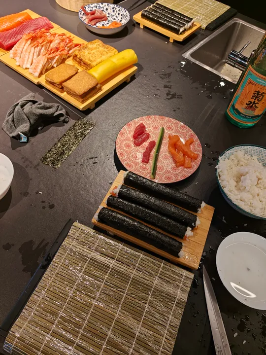 Sushi-Zutaten und -Rollen auf Küchentheke.