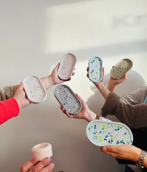 Hände halten Terrazzo-Stil-Tabletts vor Wand.