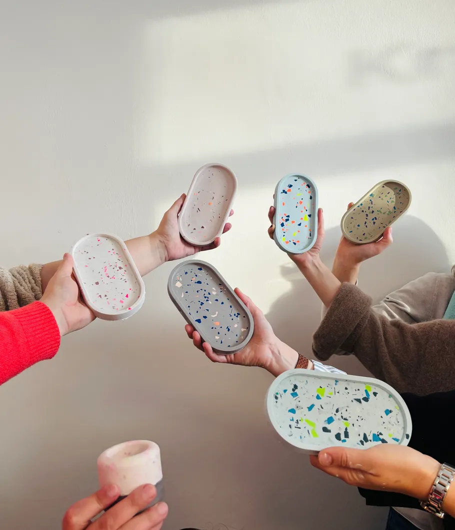 Hände halten Terrazzo-Stil-Tabletts vor Wand.