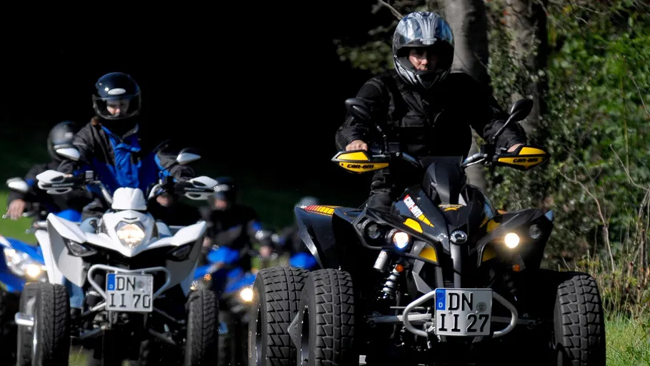 ATV riders driving on a forest path.