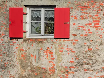 Rotes Fenster mit Blumengittern in einer Ziegelmauer.