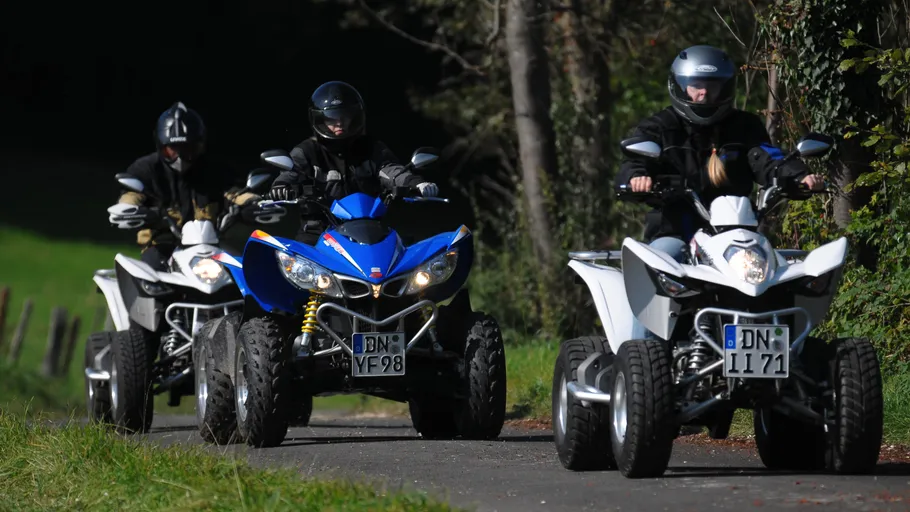 Drei Personen fahren Quads auf Asphalt.