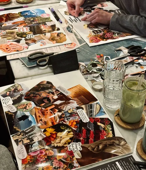 Hands making collages on a cluttered table.