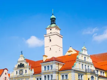Türmchen mit grünem Dach über bunten Gebäuden, blauer Himmel.
