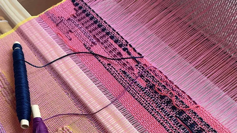 Pink and purple weaving on a loom.
