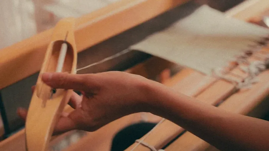 Hand operates loom shuttle weaving fabric.