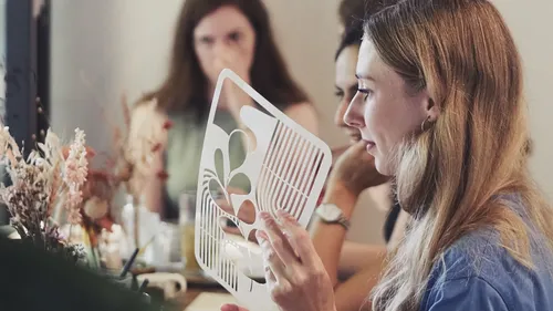 Woman holding stencil while sitting at table.