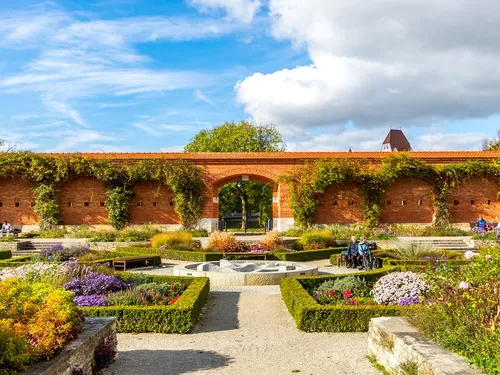 Garden with colorful flowers under blue sky and clouds.