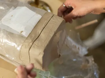Hands cutting block of clay on table.