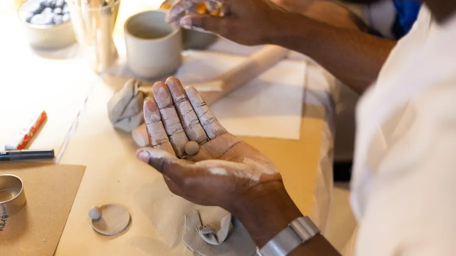 Hands molding clay on a worktable.