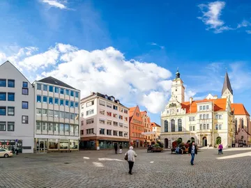 Stadtplatz mit historischen Gebäuden, Menschen gehen spazieren.