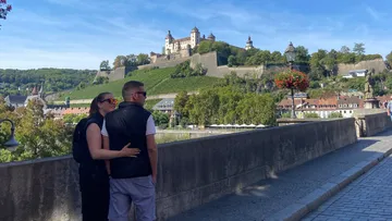 Couple embracing on bridge with castle view.
