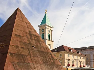 Pyramide steht, Uhrturm zeigt Zeit, klarer Himmel im Hintergrund.