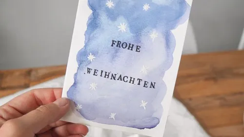 Hand holding Christmas card with blue watercolor.