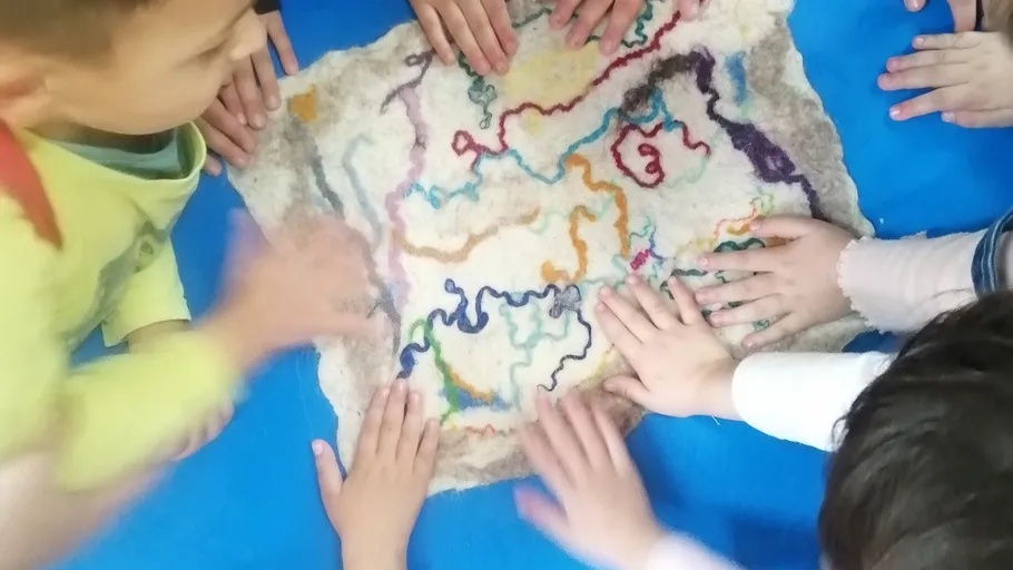 Children touch colorful felted fabric on blue mat.