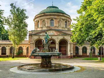 Brunnen mit Figuren, Wasser sprudelt vor historischem Gebäude.