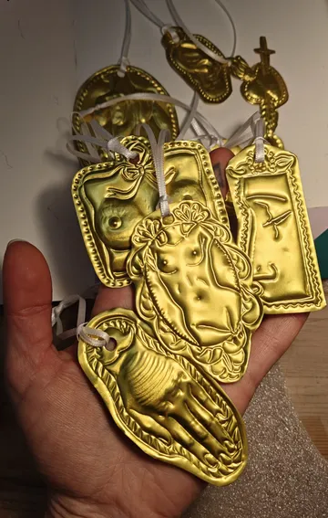 Hand holds multiple gold votive offerings.