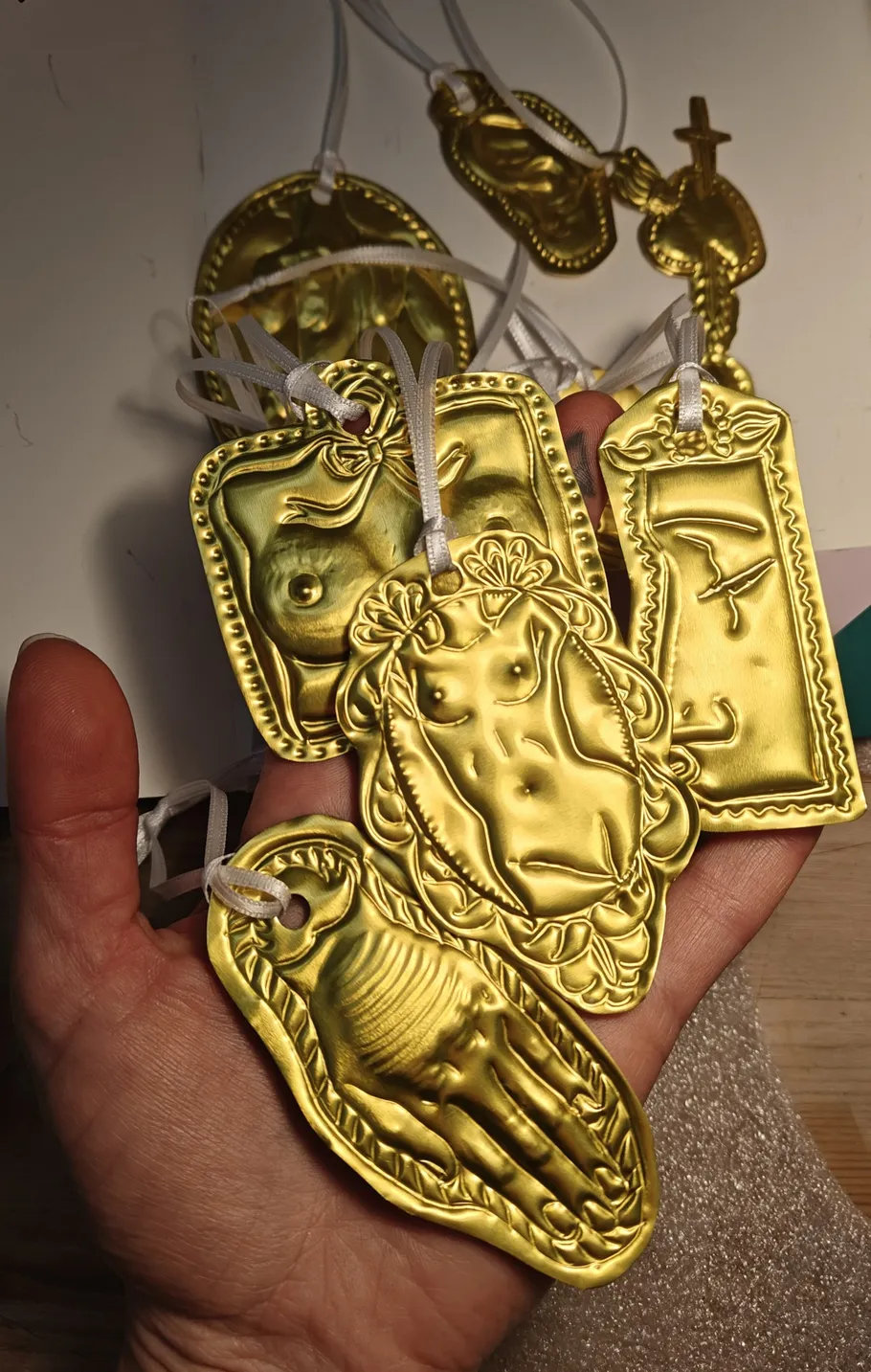 Hand hält mehrere goldene Votivgaben.