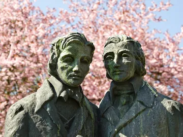 Statues of two men in front of blossoming cherry trees.