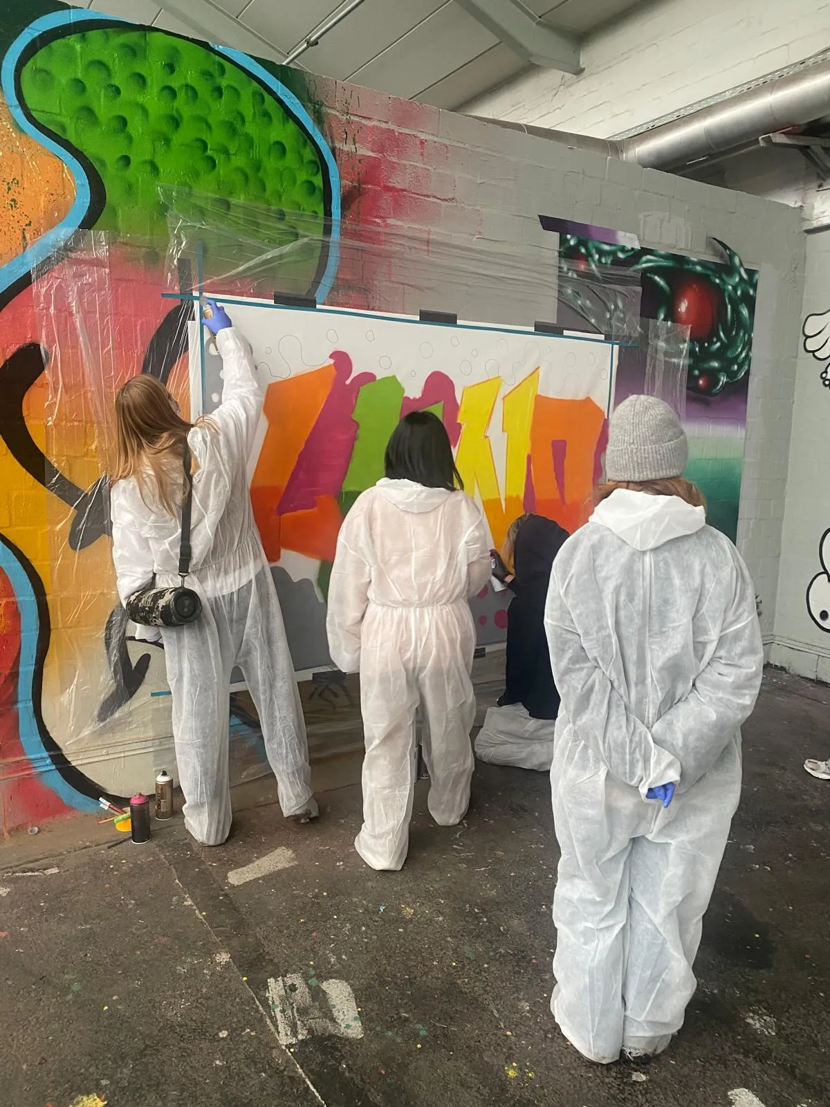 Personen sprühen Graffiti auf eine Wand.