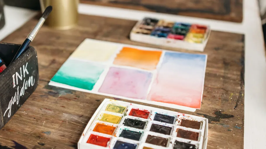 Watercolor paints with brush on wooden surface.